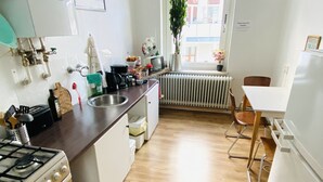 A modern kitchen with a gas stove, sink, and white cabinets. There is a radiator under the window and a chair in the corner. - Quite, artsy apartment in a central location (Hannover)