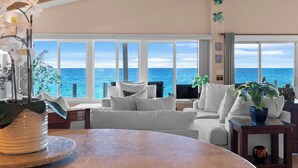 A spacious living room with a large window overlooking the sea, a ceiling fan, and a view of the ocean.