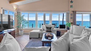 A spacious living room with a large TV, comfortable seating, a coffee table, and a view of the ocean.