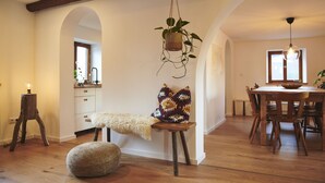 Zona pranzo con arredi in legno, una pianta sospesa e una panca con un cuscino soffice.