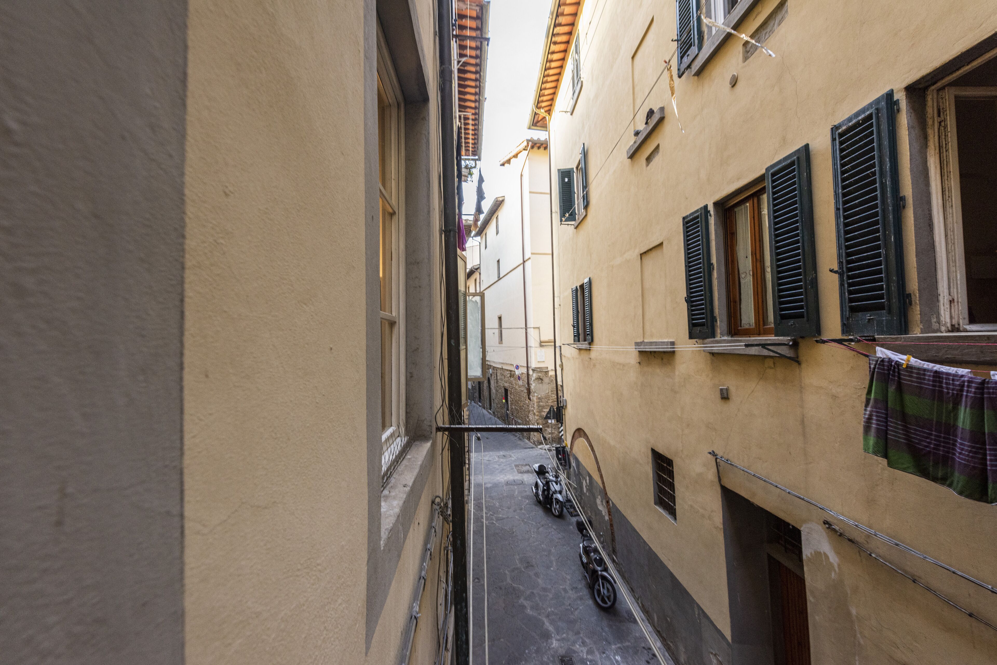 A narrow alleyway with buildings on either side, a motorcycle parked on the right, and laundry hanging on a line.