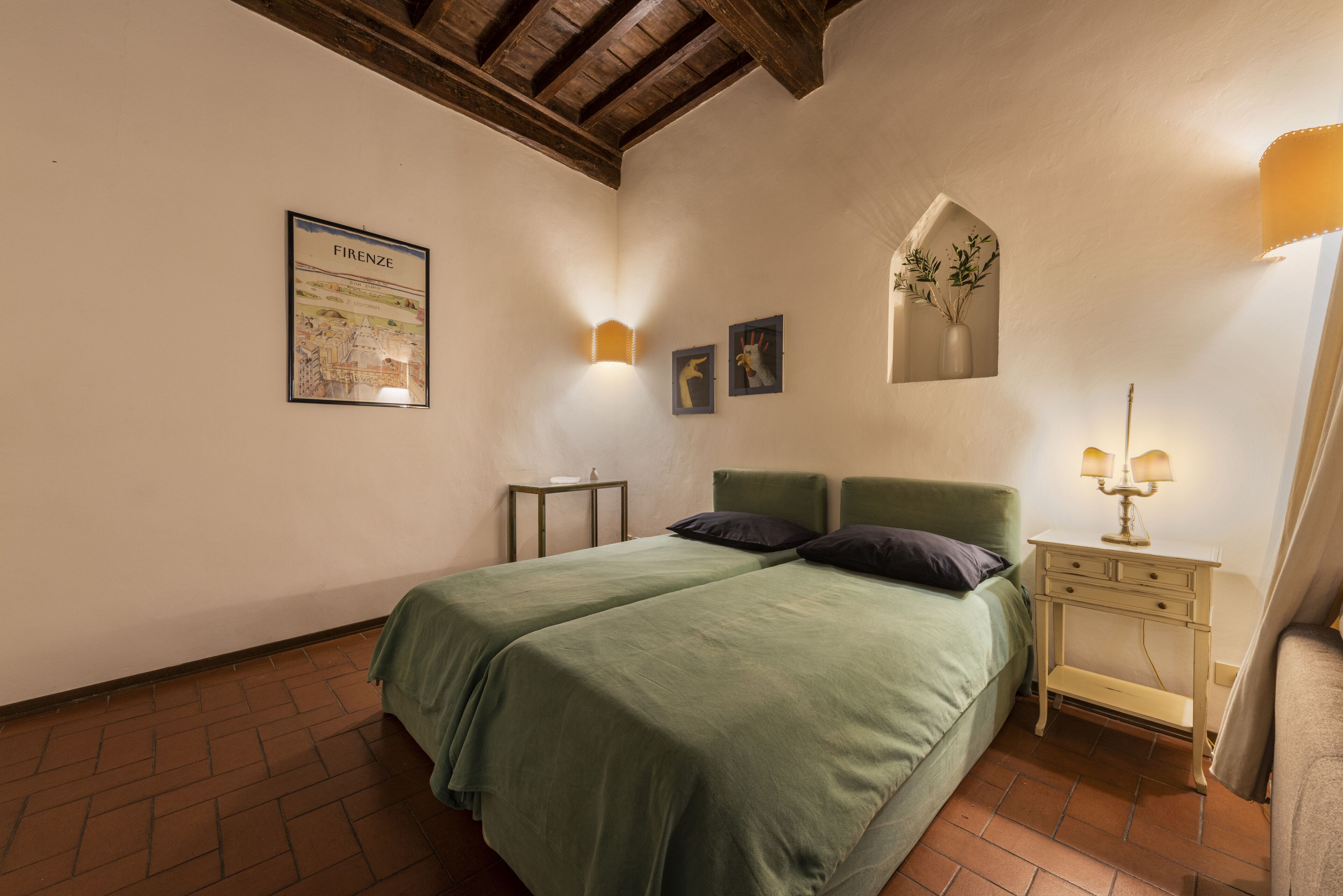 Un dormitorio con dos camas individuales, una mesita de noche, una lámpara fijada a la pared y un cuadro enmarcados de Florencia.