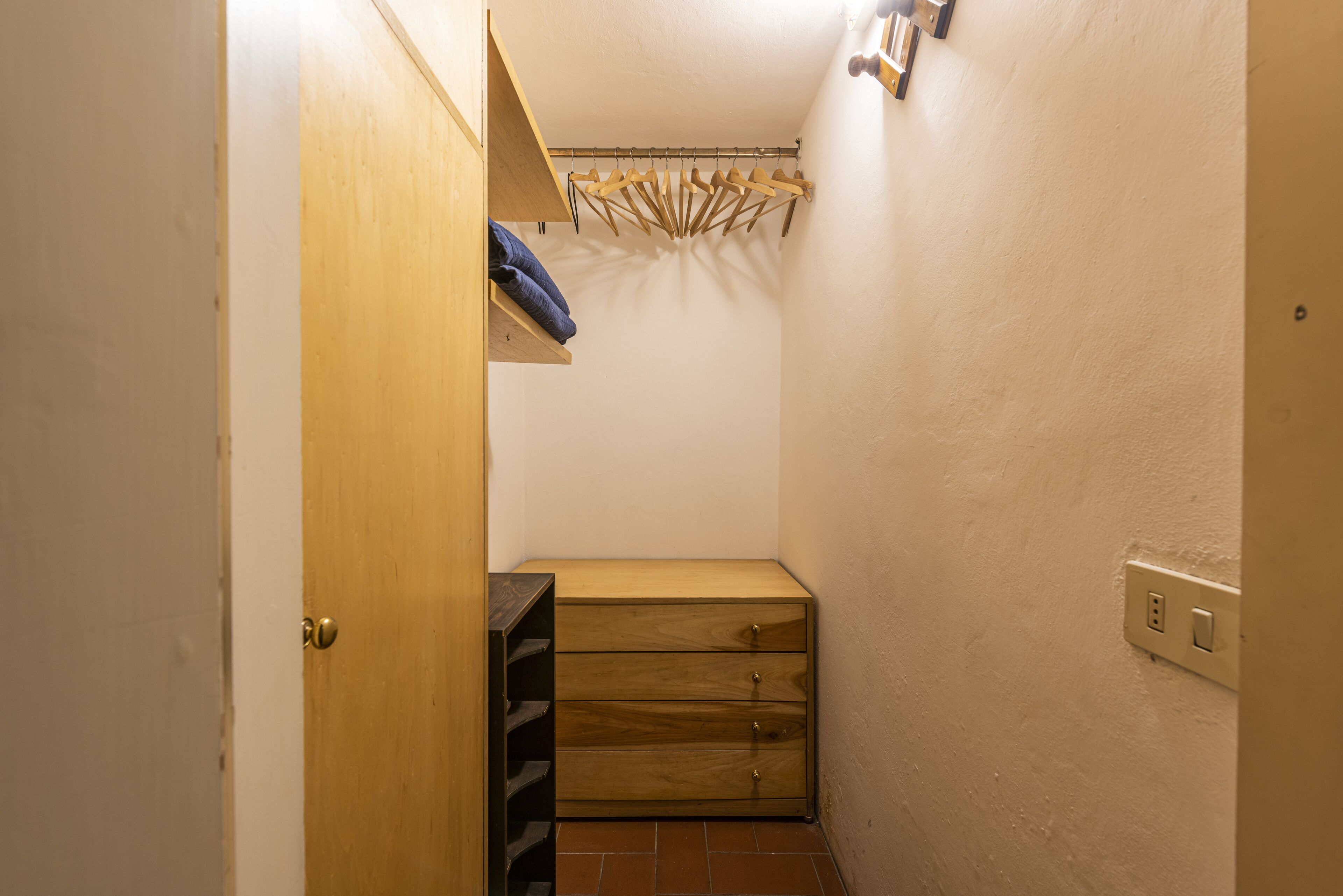 A small, narrow room with a wooden bench, a wooden shelf with a towel, and a clothes rack.
