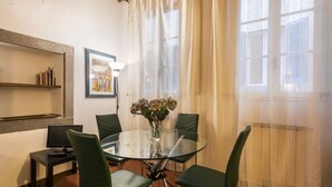 A dining area with a glass table surrounded by green chairs, a vase with flowers, a bookshelf, and a framed picture on the wall. - Pitti Studio by Mmega (Florence)