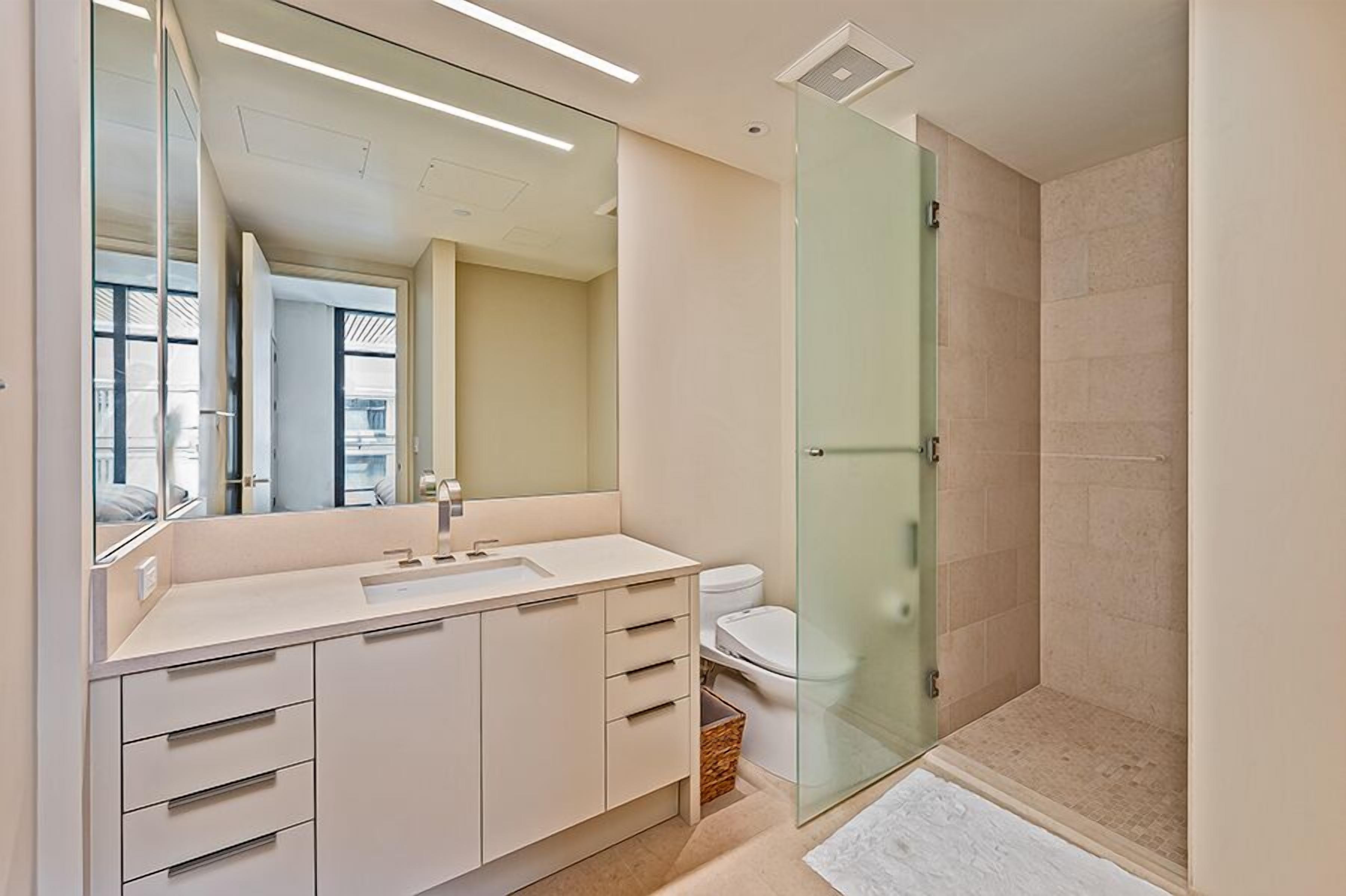 Un baño moderno con un espejo grande, un lavabo y una ducha con mampara de cristal.