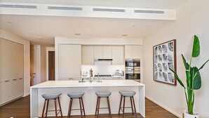 A modern kitchen with a central island, bar stools, and a large potted plant.