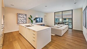 A modern kitchen with a central island, a dining area with a sofa, and a large window offering a view of the outside.