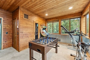 Habitación con piso de madera, una mesa de fútbol de mesa, una cinta de correr y otra mesa de fútbol de mesa con el logotipo 'GD'.