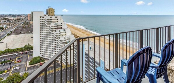 A high-rise hotel overlooking a beach with a clear view of the ocean and a parking lot.