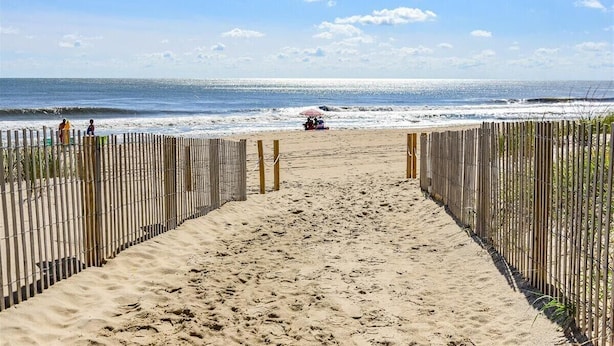 Ein Sandweg am Strand, gesäumt von einem Holzzaun auf beiden Seiten, der zum Meer führt.