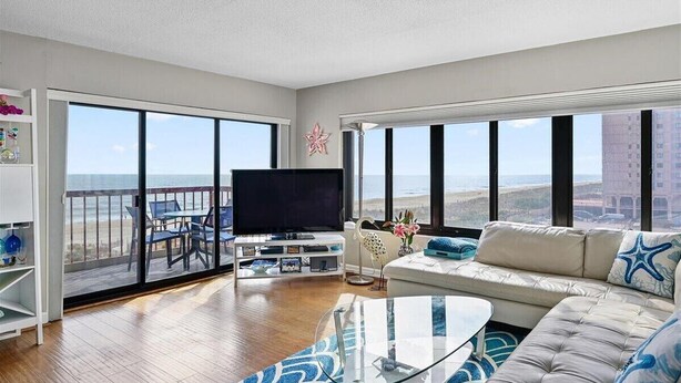 Un salon spacieux doté d’une grande télévision, de sièges confortables et d’un balcon offrant une vue sur l’océan.
