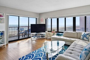 Un salon spacieux doté d’une grande télévision, de sièges confortables et d’un balcon offrant une vue sur l’océan.