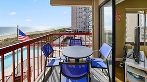 Un balcon avec vue sur la plage et l’océan, une piscine et une table avec des chaises.