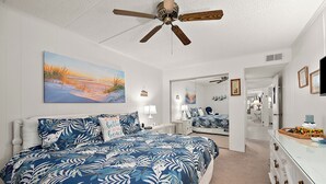Un dormitorio con una cama grande, un ventilador de techo, un cuadro y un pasillo que conduce a otra habitación.