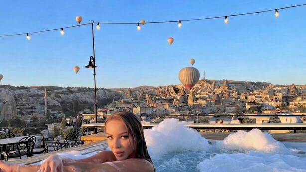 Iemand ontspant in een jacuzzi met een stadsgezicht en luchtballonnen op de achtergrond.