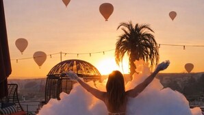Iemand in een jacuzzi met een zonsondergang en palmbomen op de achtergrond.