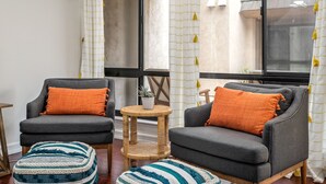 Ein gemütliches Wohnzimmer mit zwei grauen Sesseln, einem kleinen runden Tisch und einem gestreiften Hocker.
