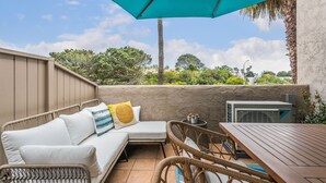 Eine Terrasse mit einem Korbsessel, einem Holztisch und einem blauen Sonnenschirm.