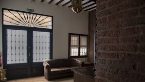 Quarto com uma porta grande identificada com 'SALIDA', um sofá de couro marrom, uma pequena mesa e uma parede de tijolos.