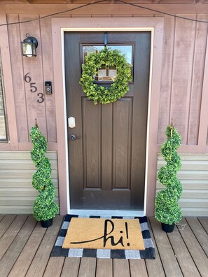 A brown front door with a wreath, a doormat with "hi!", and two small potted plants on either side. - The Cozy Pinetop Cottage with hot tub (Lakeside)