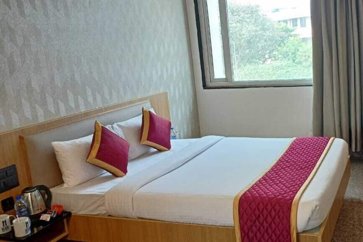 A hotel room with a bed, a desk, a TV, and a window with curtains.