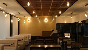 Een restaurant met hoge plafonds, hangende lampen en een combinatie van zitbanken en tafels.