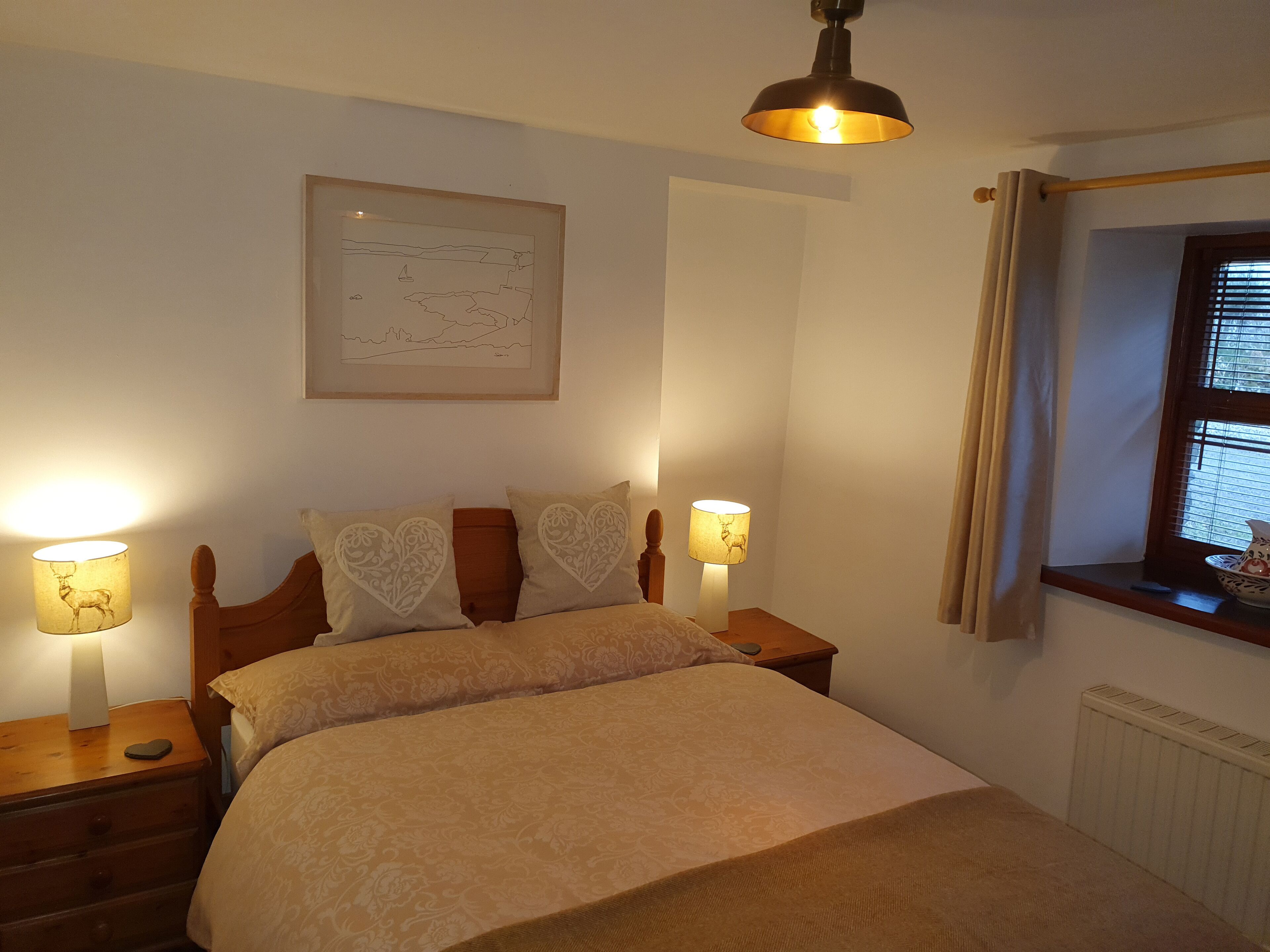 A neatly arranged bedroom with a bed, two bedside lamps, a framed map on the wall, and a window with curtains.