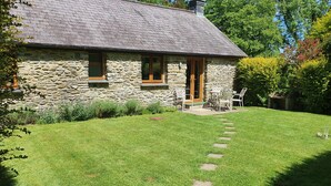 Une maison en pierre avec une pelouse verdoyante et un chemin de pierres menant à une porte en bois.