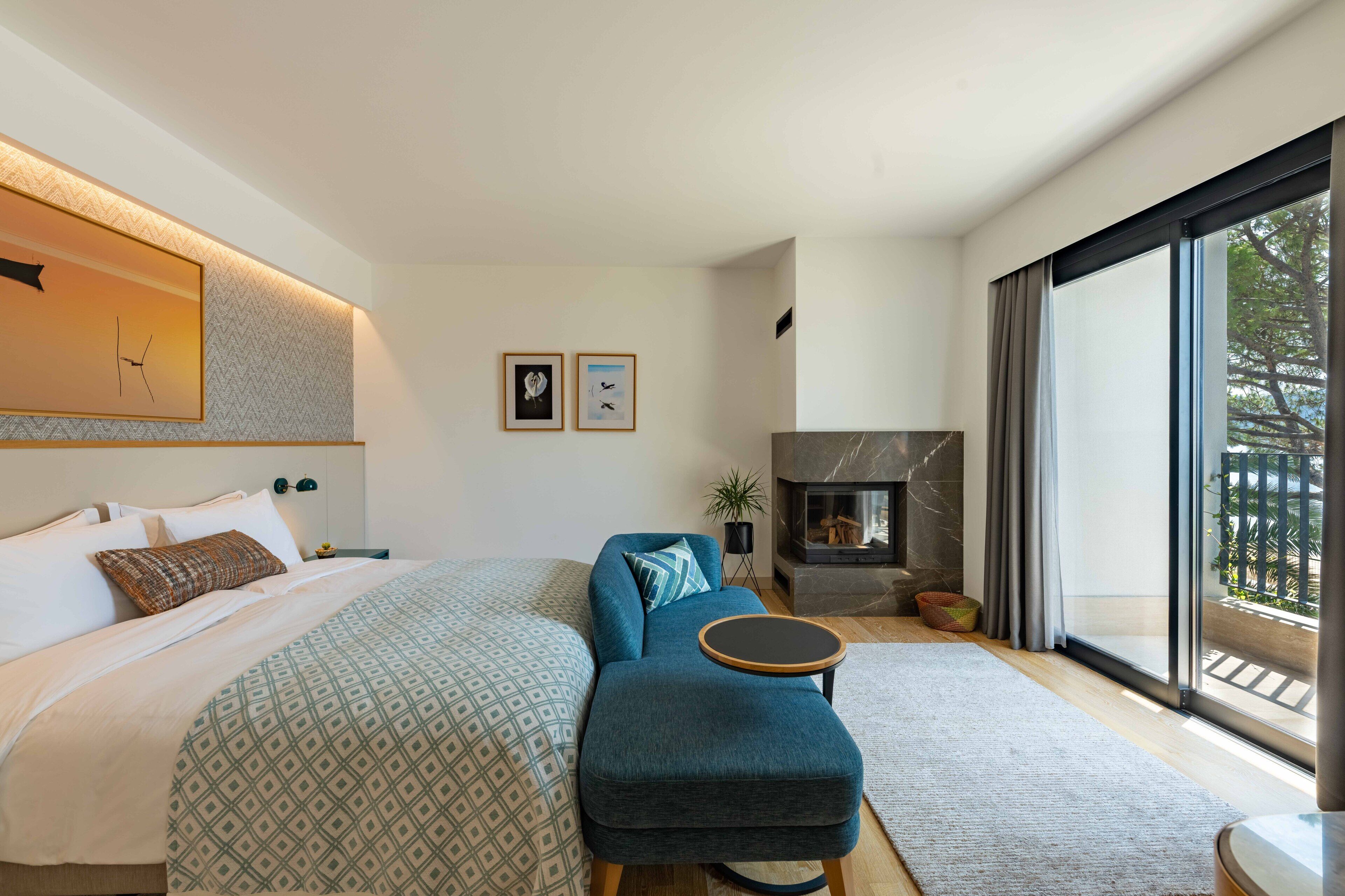 A modern bedroom with a large bed, a sofa, a small table, and a fireplace.