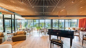 A spacious lobby with a grand piano, wooden ceiling, large windows, and modern furniture.