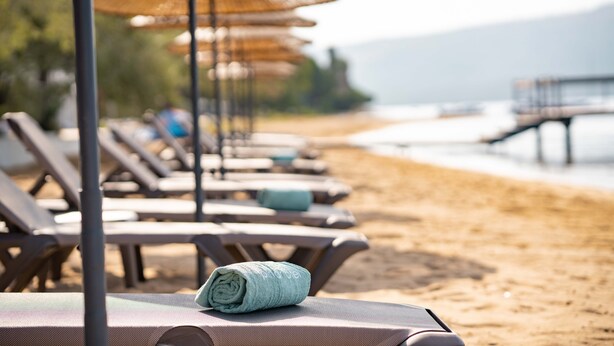 A row of sun loungers with towels, beach umbrellas, and a view of the beach and water.