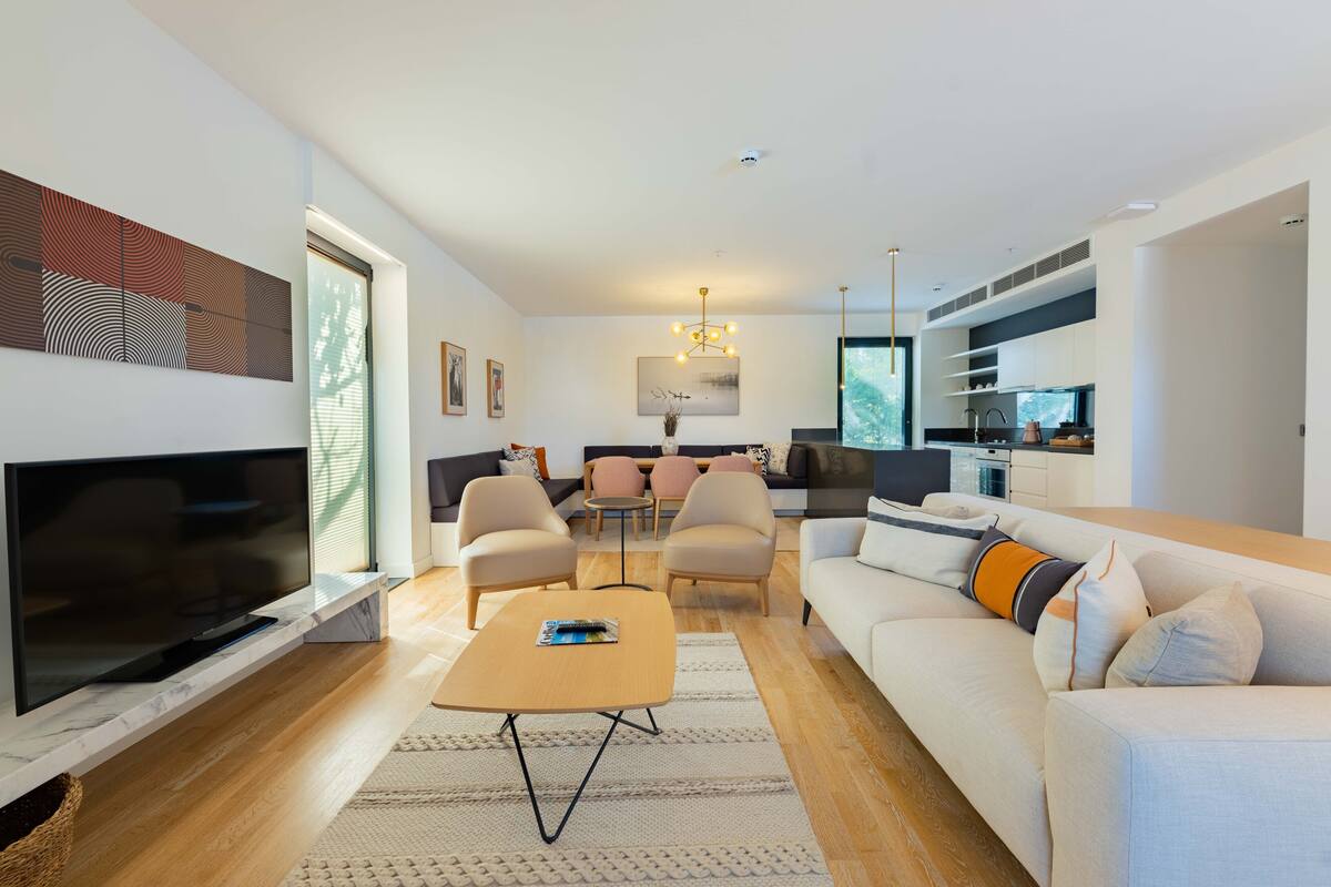 A modern living room with a flat-screen TV, a sofa, a coffee table, and a dining area with chairs.