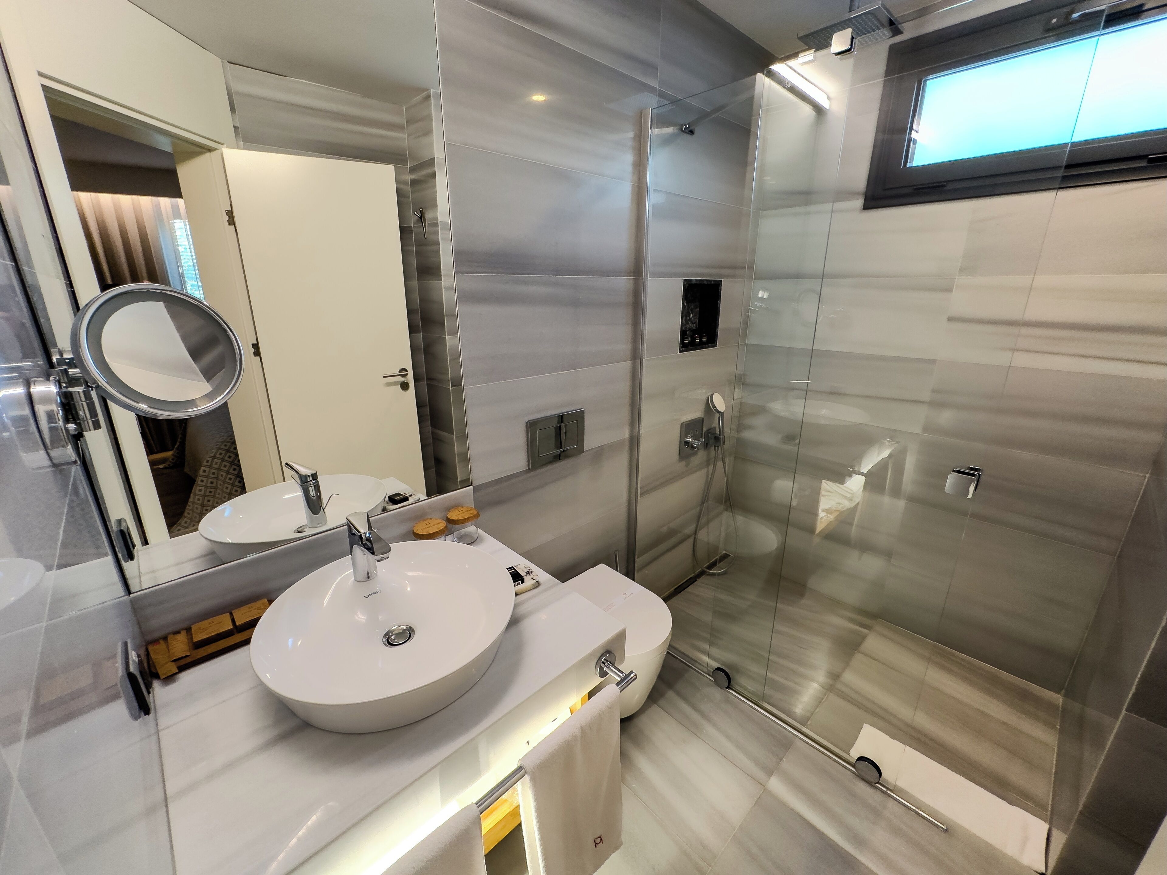 A modern bathroom with a glass shower enclosure, a round mirror, and a white sink.