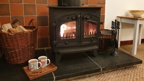 A wood-burning stove with a basket of firewood and two mugs on a tray. - Ty Twt (Lampeter)
