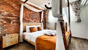 Une chambre avec un mur en briques, un cadre de lit en bois, une table de chevet et un lit à baldaquin surmonté d’un ciel de lit blanc.