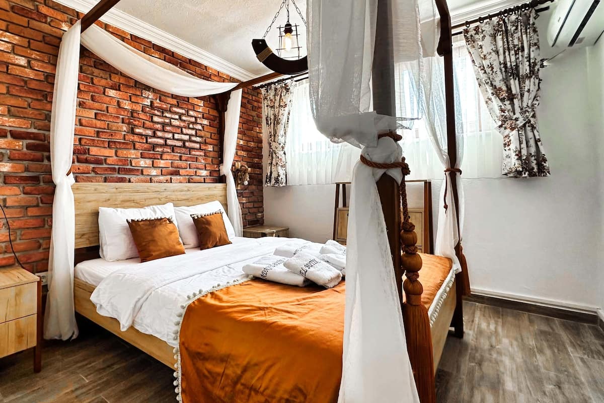A bedroom with a brick wall, a wooden bed frame, a nightstand, and a canopy bed with a white canopy.