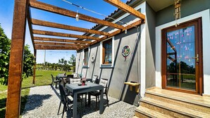 Une terrasse couverte avec des meubles d’extérieur, une pergola en bois et une grande fenêtre agrémentée d’éléments décoratifs.