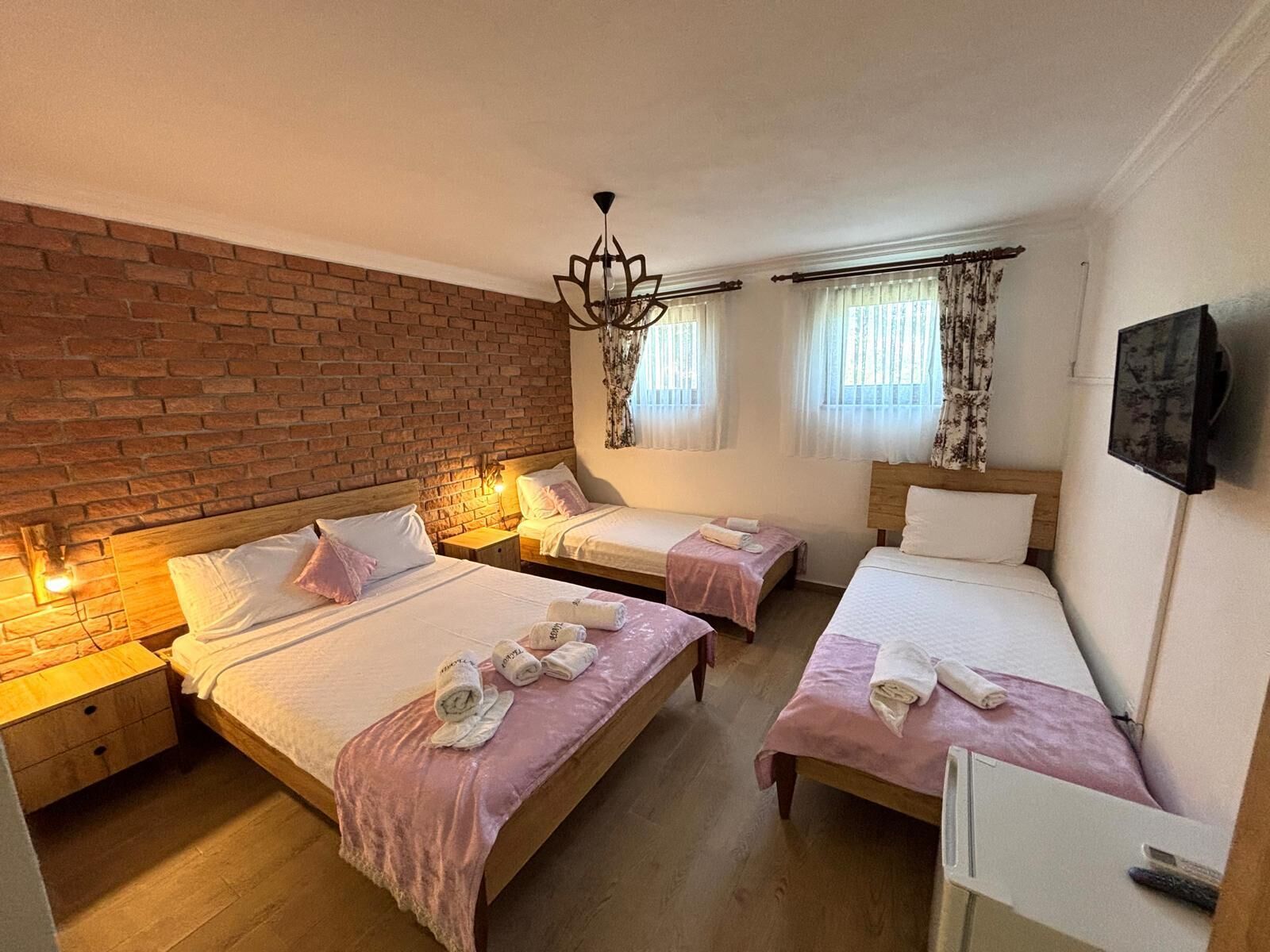 A hotel room with four beds, a brick wall, a chandelier, and a TV on the wall.