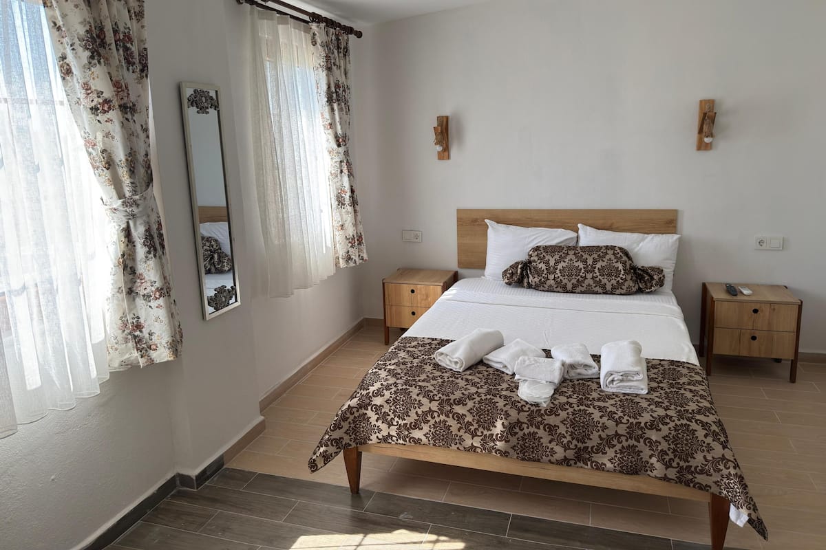 A hotel room with a bed, two bedside tables, a wooden headboard, a mirror, and curtains.