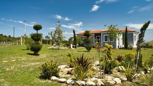 Une maison moderne à deux étages, avec un toit recouvert de tuiles rouges, entourée d’une pelouse bien entretenue et de divers arbustes.
