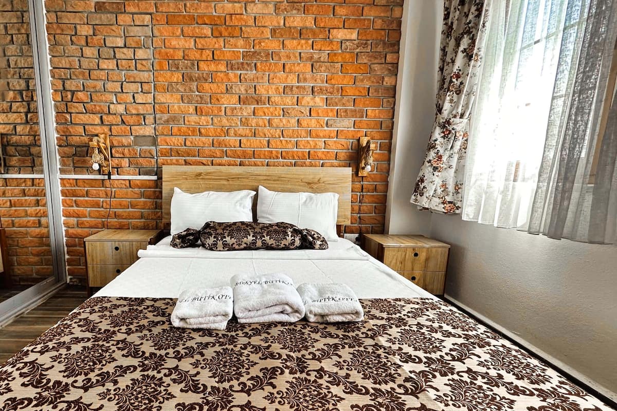 A hotel room with a brick wall, a wooden bed, white bedding, and a patterned bedspread.