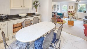A modern kitchen with white cabinets, a marble countertop, and a dining area with a white table and wicker chairs. - Host & Stay | Rose Cottage (Middlesbrough)