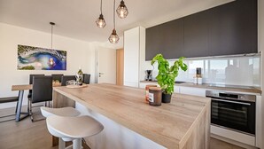 Una cocina moderna con una isla de madera, taburetes de bar, una planta de albahaca en maceta grande y un horno de acero inoxidable.