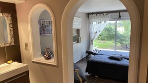 Quarto com cama, uma cadeira, um espelho e janela com vista para o verde.