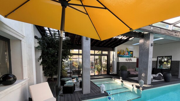 Área de piscina com espreguiçadeiras, um guarda-sol amarelo e vista para o exterior.