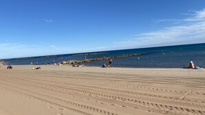 Uma praia arenosa com pegadas e um paredão rochoso ao fundo.