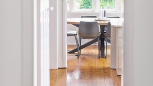 A modern kitchen with white cabinets, a wooden floor, and a dining area with chairs and a table. - Heritage on Hill - Refreshing Elegance (Orange)