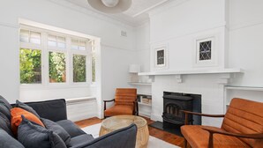 A living room with a fireplace, a sofa set, and a window with a view of greenery. - Heritage on Hill - Refreshing Elegance (Orange)
