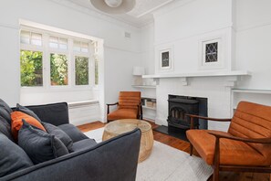 A living room with a fireplace, a sofa set, and a window with a view of greenery.