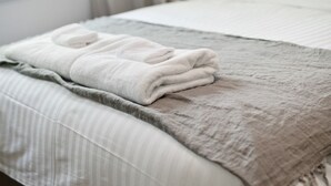A neatly made bed with a folded white towel, a grey blanket, and striped bedding. - Heritage on Hill - Refreshing Elegance (Orange)